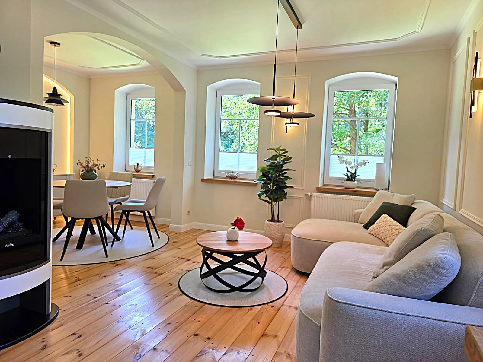 Ferienwohnung 2 Schwarzmühle — Wohnzimmer mit Kamin, Essbereich und Fenstern